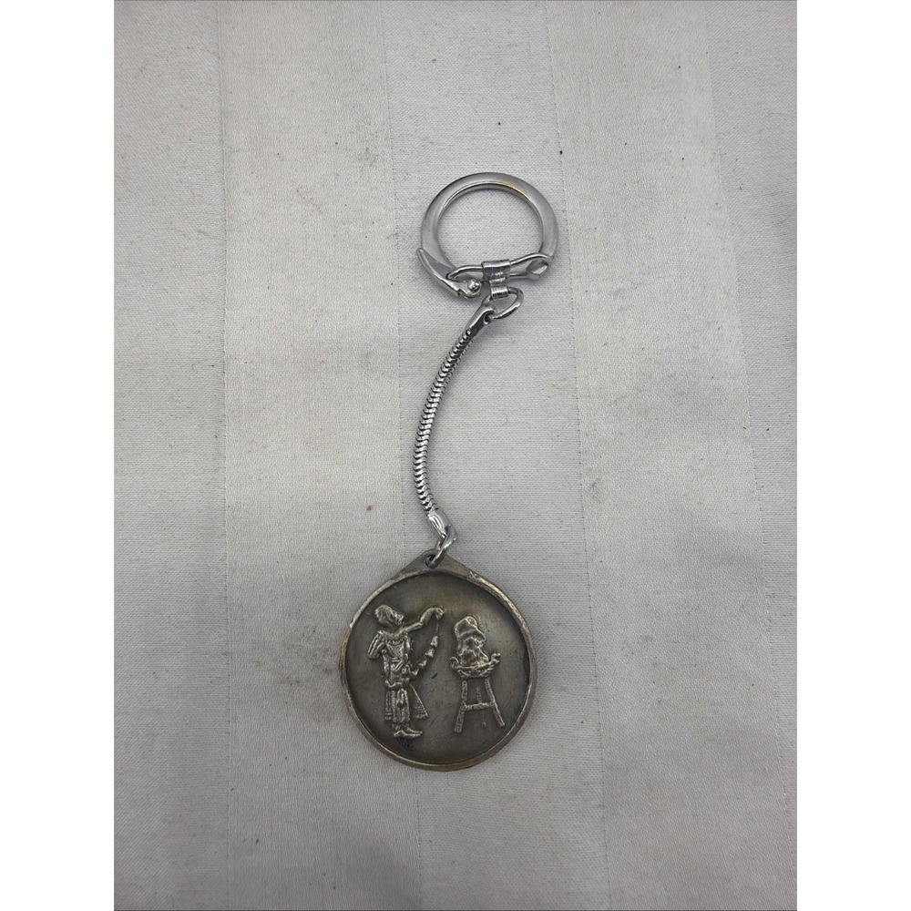 silver-toned keychain with a round charm featuring a detailed relief scene